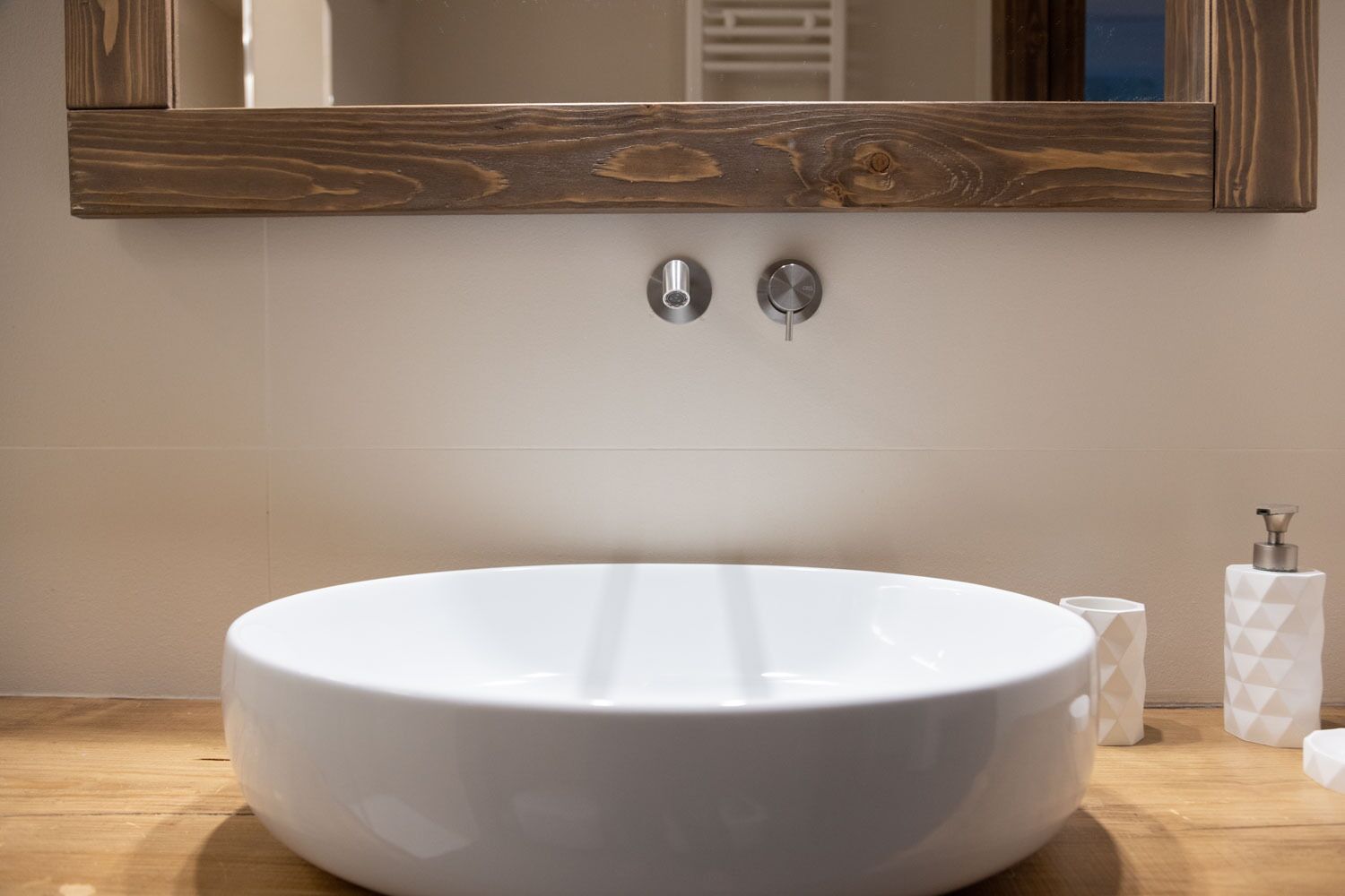 Une salle de bain avec un grand lavabo blanc, un miroir encadré en bois et un distributeur de serviettes.