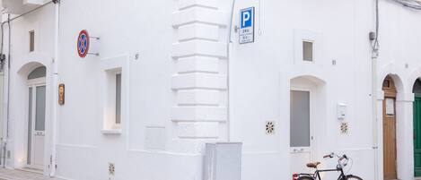 A white building with a bicycle parked outside, a no parking sign, and a blue parking sign.