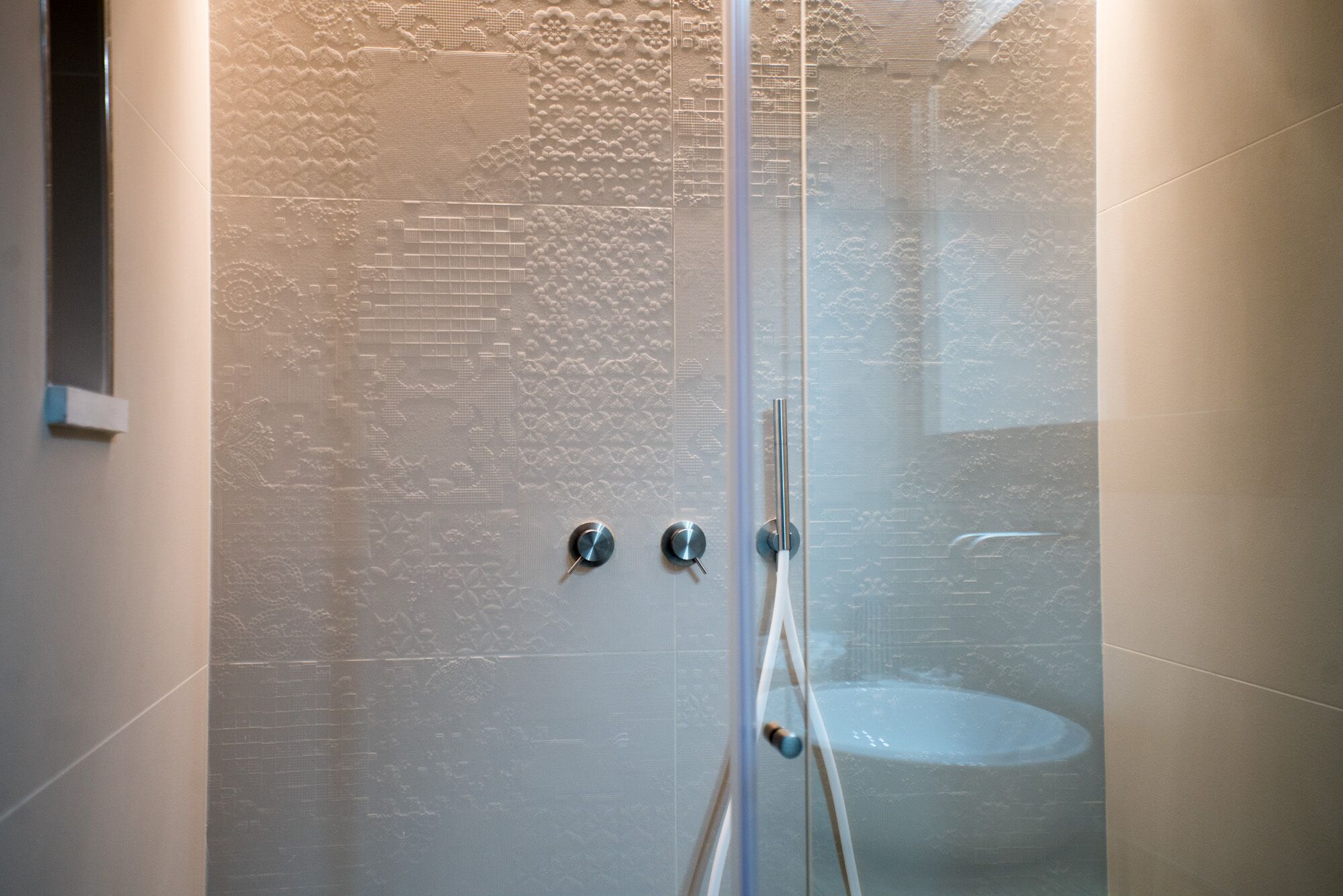 A glass-enclosed shower with a textured wall, a faucet, and a handheld showerhead.