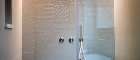 A glass-enclosed shower with a textured wall, a faucet, and a handheld showerhead.