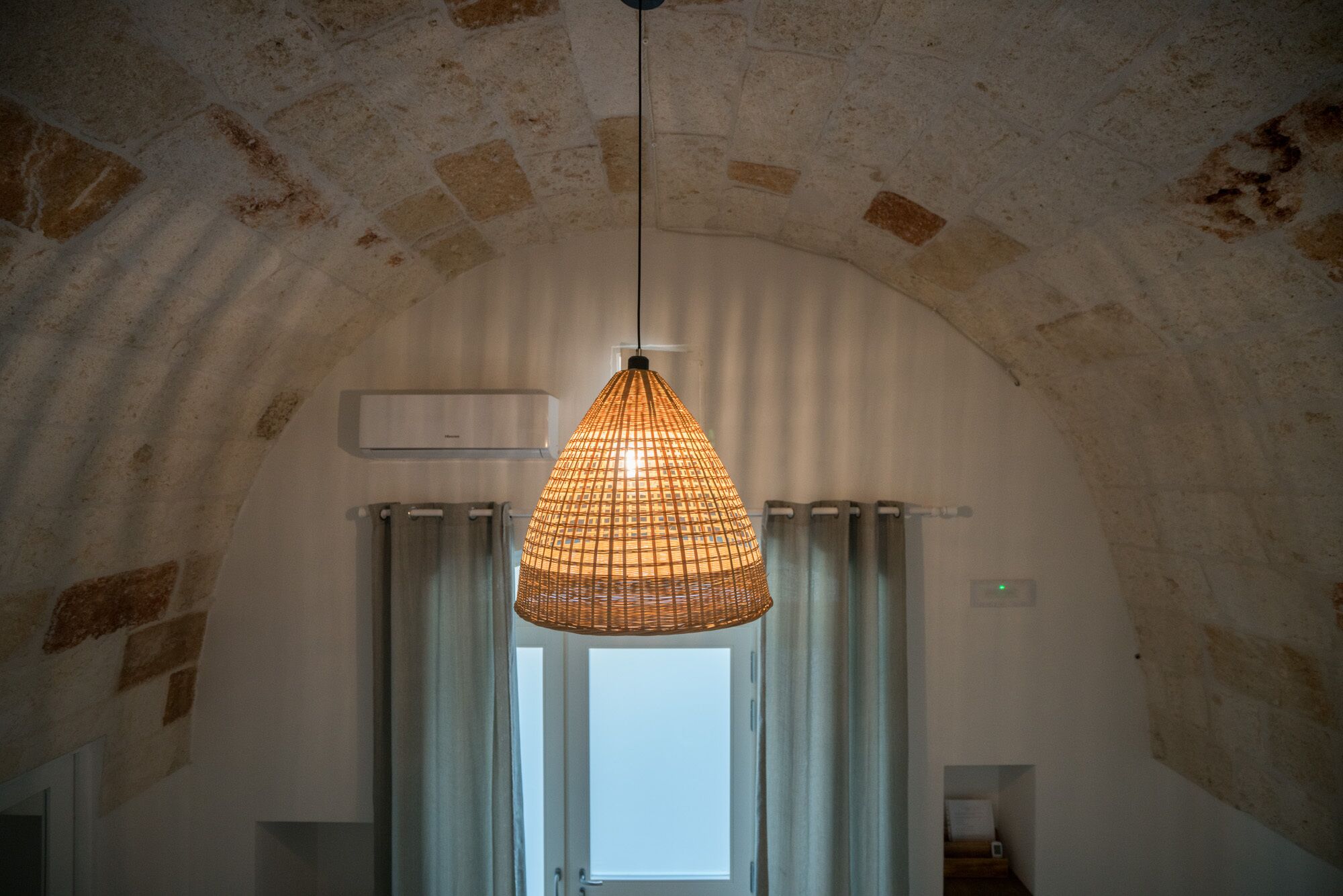 Een kamer met een hoge gewelfde plafond, een hangende geweven lamp en een raam met gordijnen.