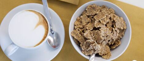Una taza de café, una cuchara y un tazón de cereal sobre una mesa.
