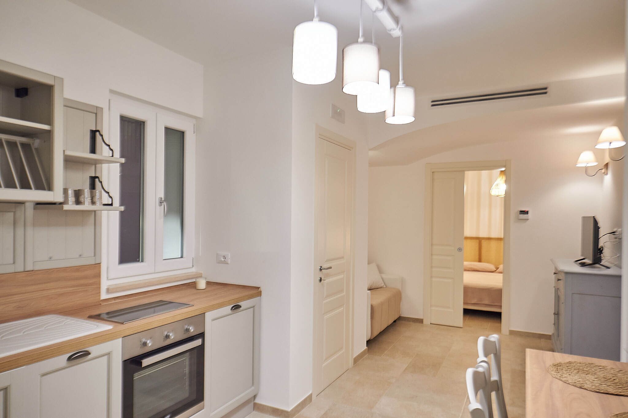 A modern kitchen with white cabinets, a wooden countertop, and pendant lighting.