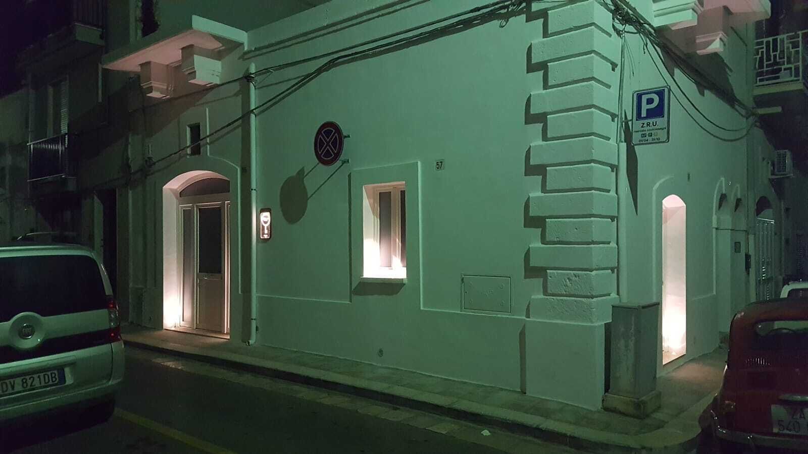 Un edificio con una puerta, un ventanal pequeño, un letrero de estacionamiento y el número 57 en la pared.
