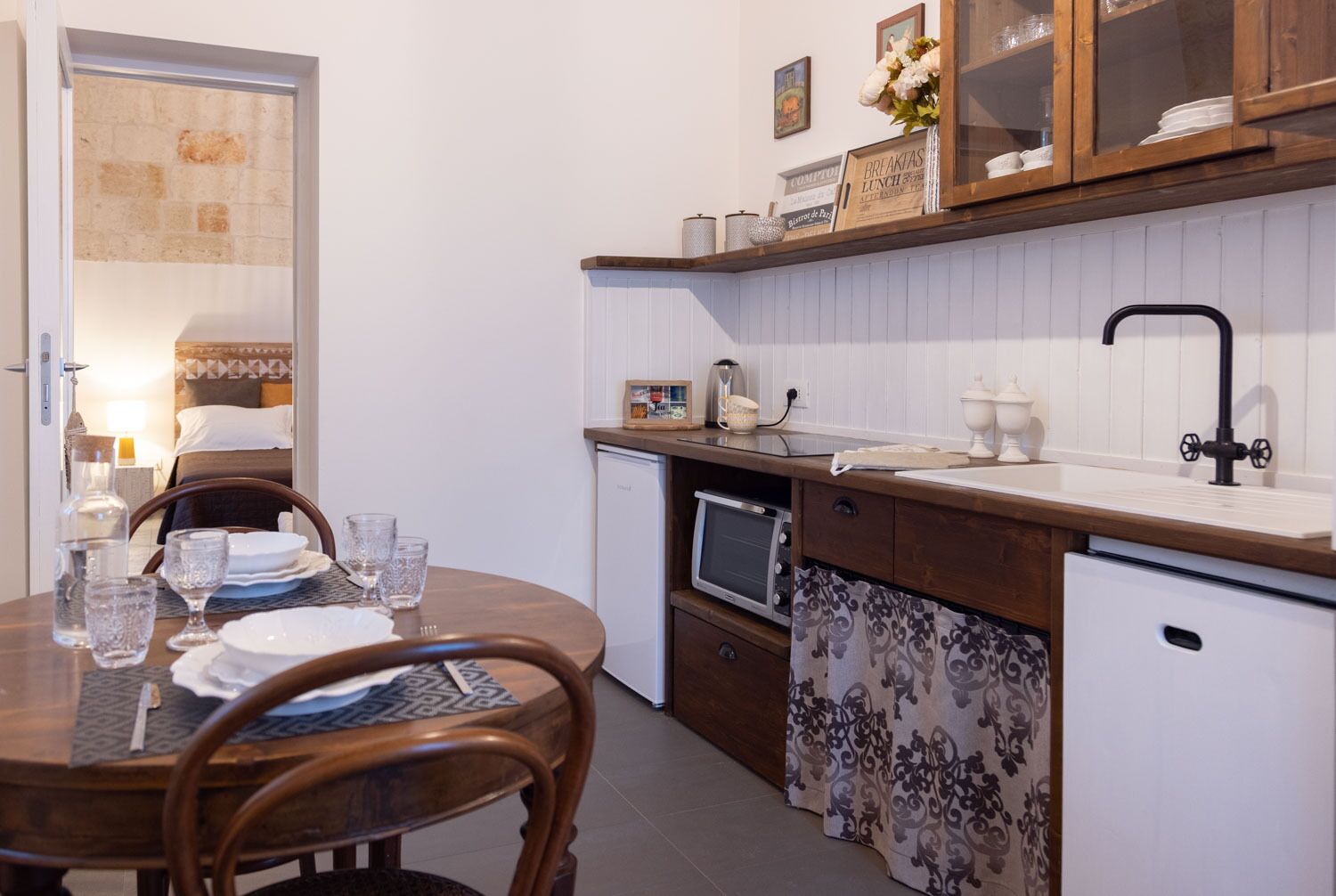 Una cocina compacta con una mesa de comedor para dos personas, microondas, fregadero y un refrigerador pequeño.