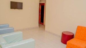 A hallway with a TV mounted on the wall, a red door at the end, and seating areas with blue and orange chairs. - Kedros Precious Suites (Ilorin)