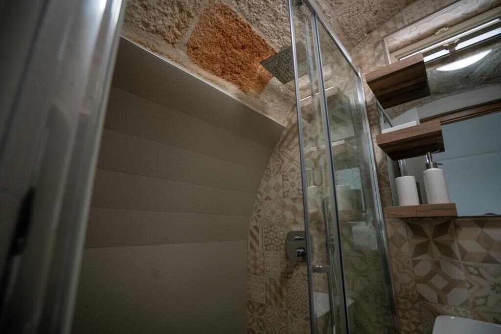 Un baño con baldosas estampadas, cabina de ducha de vidrio y un estante de madera con artículos de aseo.