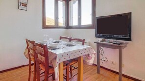 Un coin repas avec une table dressée pour quatre personnes, un téléviseur posé sur un meuble et une fenêtre donnant sur une colline.