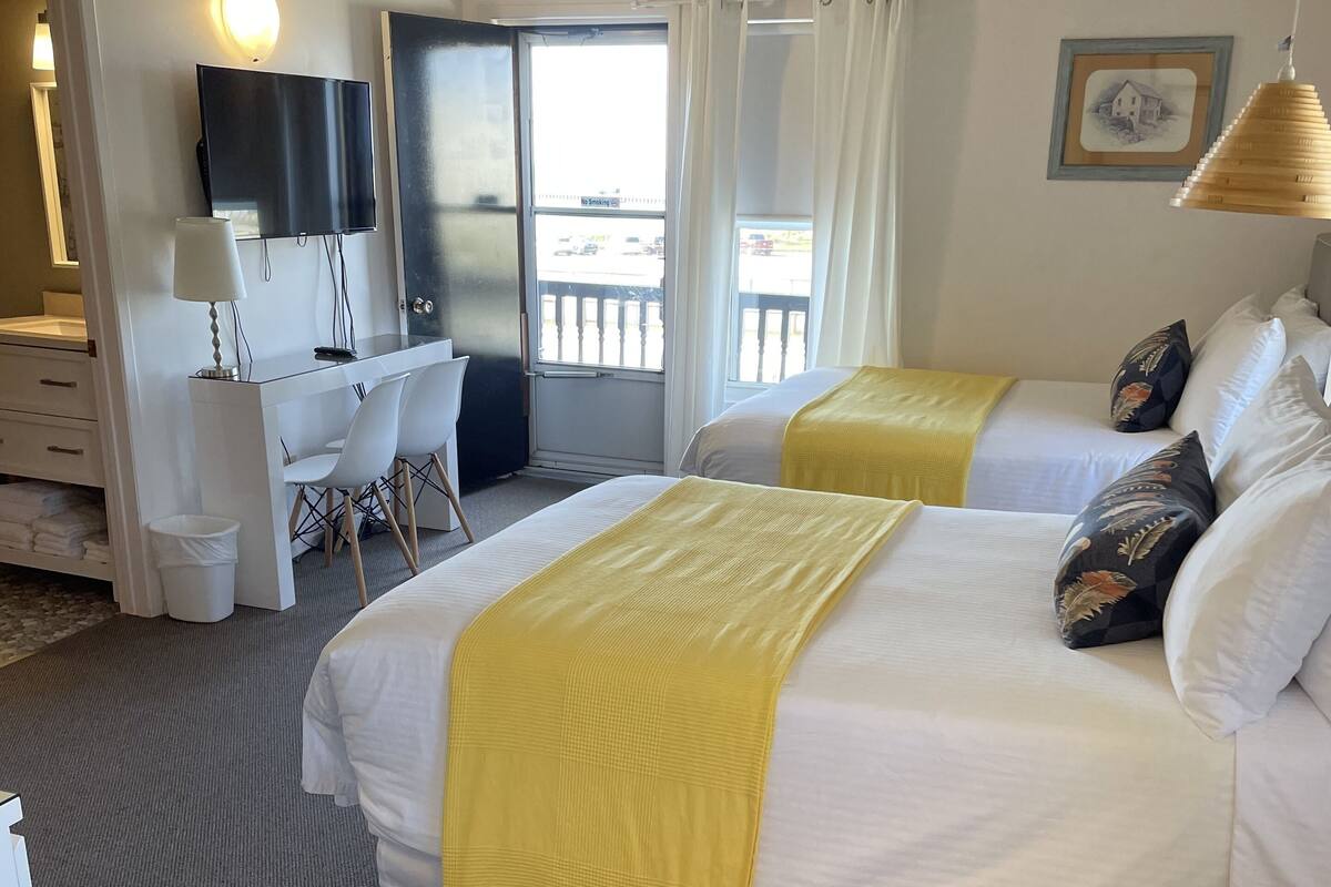 A hotel room with two beds, a desk, a chair, and a television.