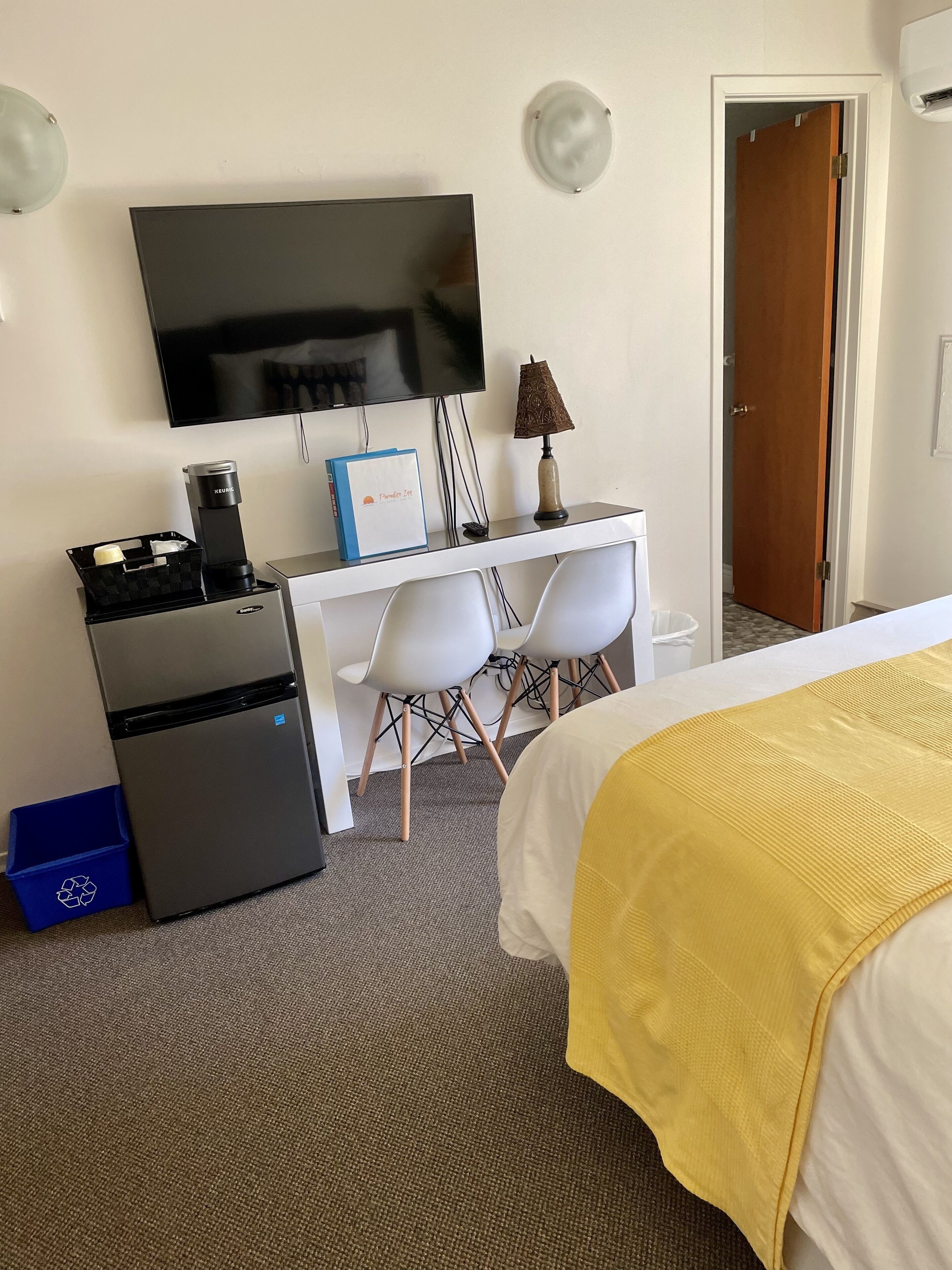 A hotel room with a bed, a desk, a television, a coffee machine, and a door.