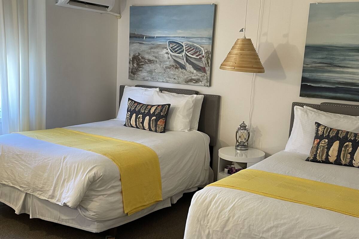 A hotel room with two beds, a nightstand, a lamp, and artwork on the walls.