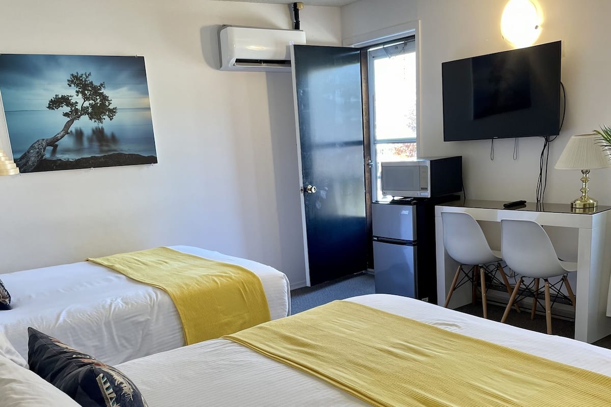 A hotel room with two beds, a desk with a chair, a TV, and a painting on the wall.
