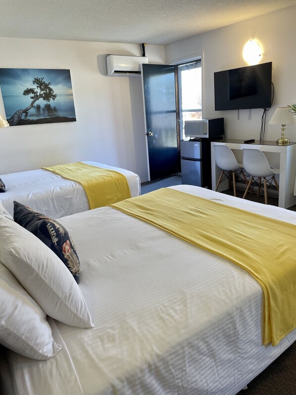 A hotel room with two beds, a desk with a chair, a TV, and a painting on the wall. - Paradise Inn On The Beach (Saugeen Shores)