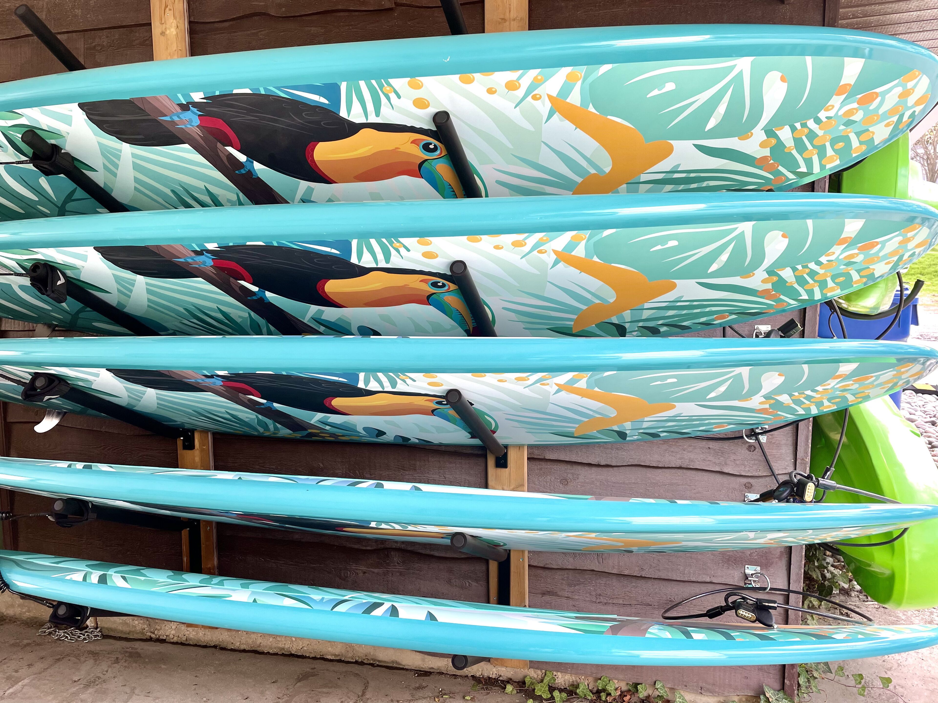 Une rangée de kayaks aux motifs tropicaux, appuyés contre une structure en bois.