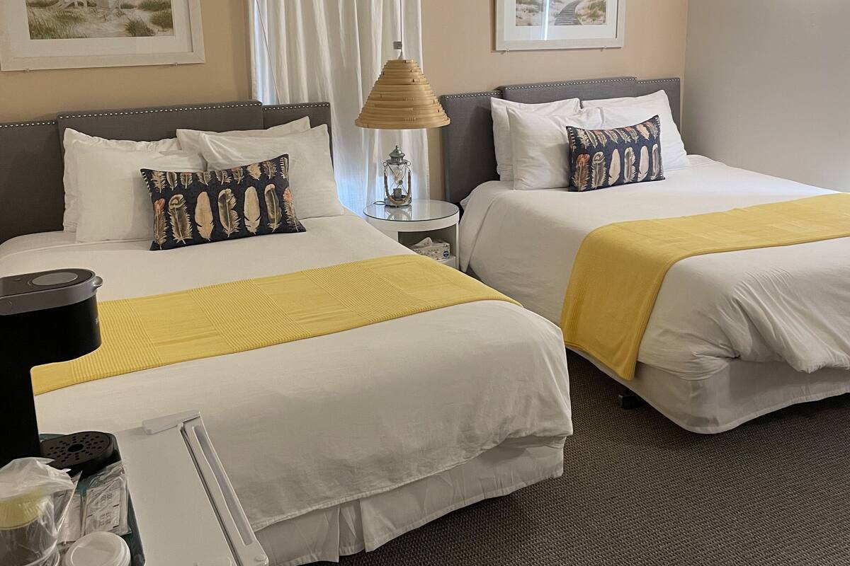 A hotel room with two beds, a desk, a lamp, and two framed pictures on the walls.