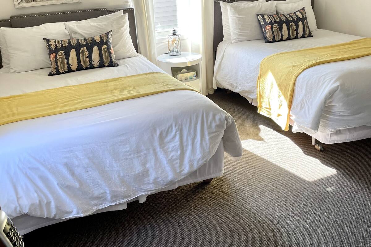 A hotel room with two beds, a small table, and a lamp.