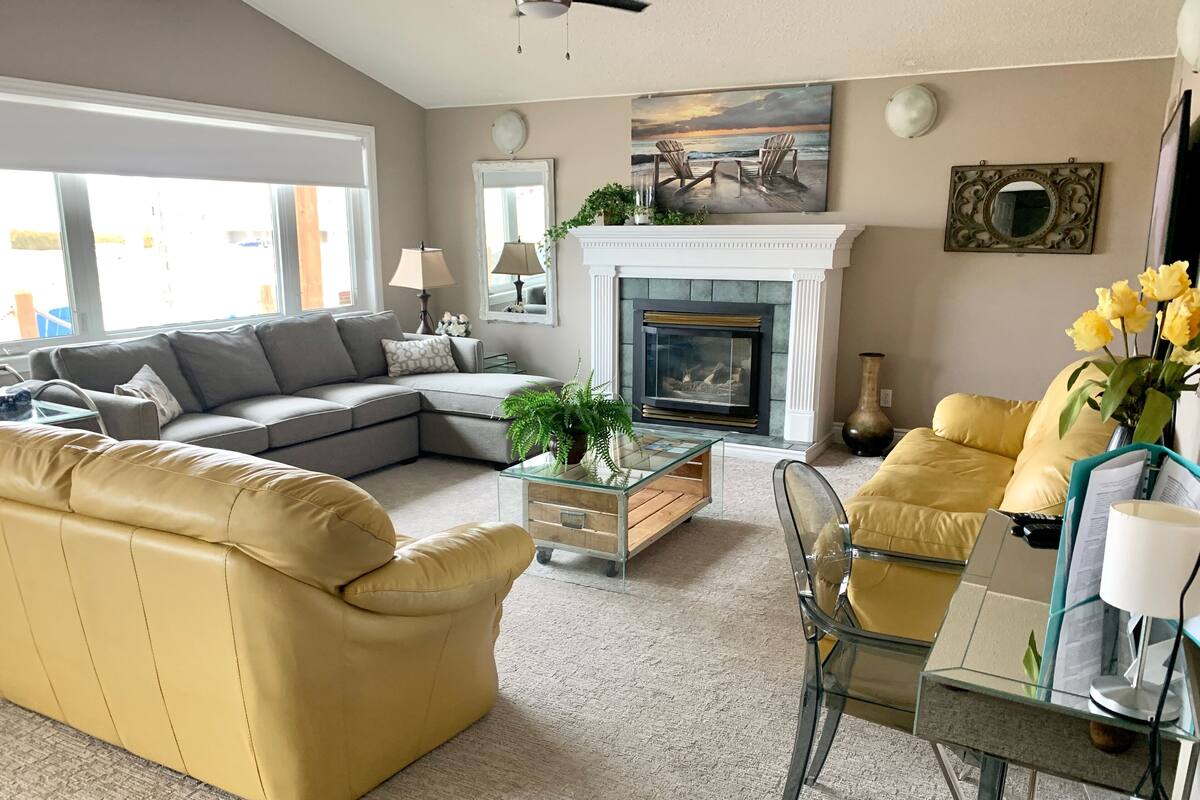 A living room with a sectional sofa, a glass coffee table, a fireplace, and a yellow armchair.