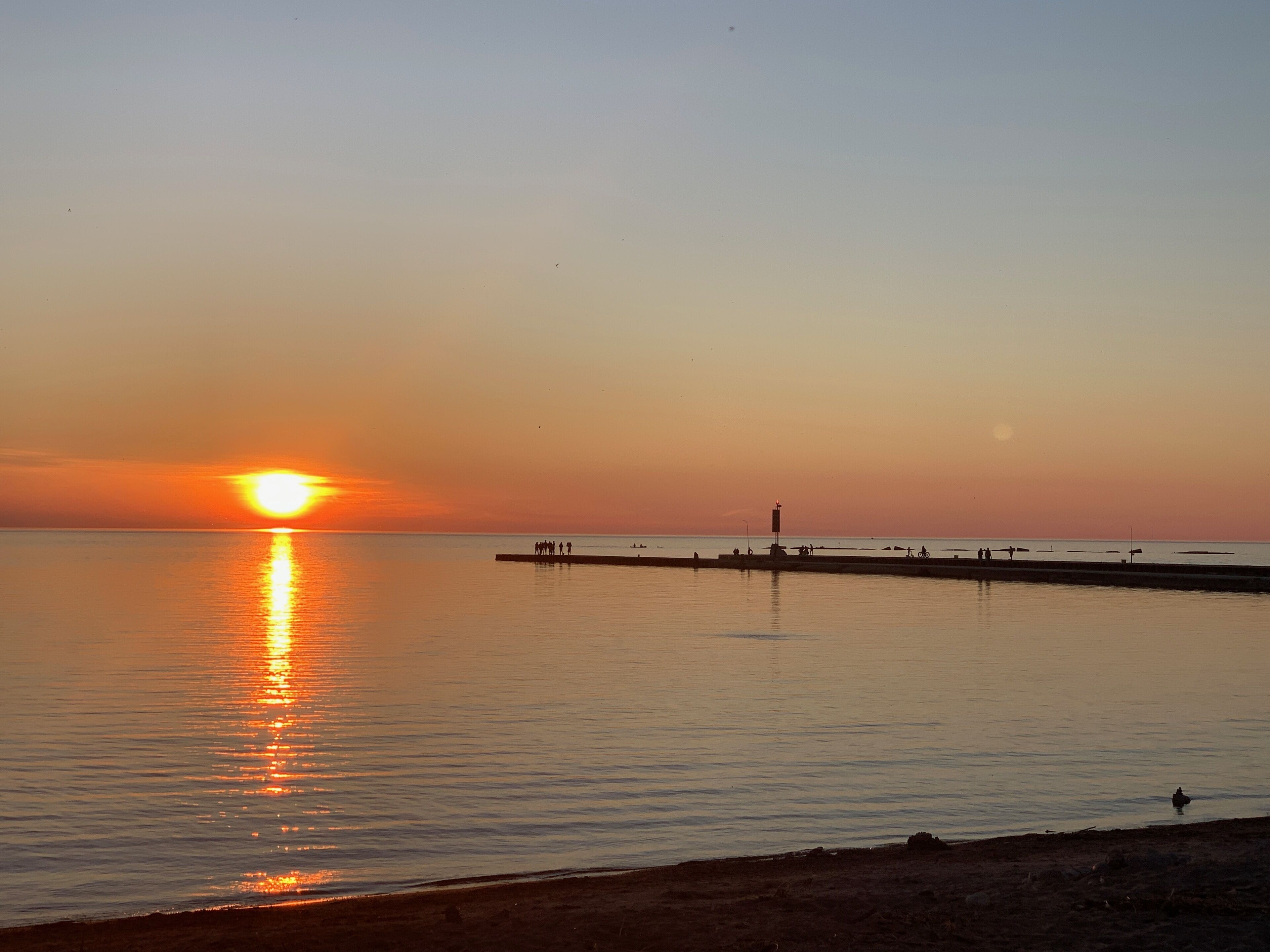 Un atardecer sobre una superficie de agua tranquila, con un muelle que se adentra en el agua.