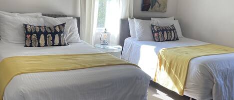 Habitación de hotel con dos camas, una ventana con cortinas, un cuadro en la pared y un equipo de aire acondicionado.