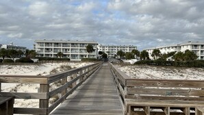Un muelle de madera que conduce a una zona de playa, con edificios al fondo.