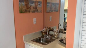 Una cocina con un lavamanos, armarios y una encimera. Hay dos cuadros en la pared sobre el lavamanos.