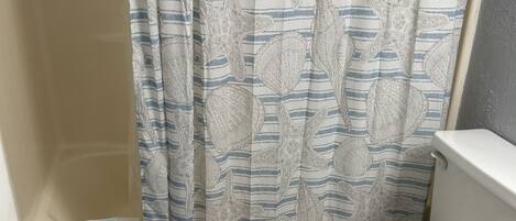A bathroom with a toilet, a shower curtain with a striped pattern, and a blue mat with the word "RELAX" on it.