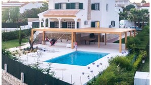 Ein zweigeschossiges Haus mit Swimmingpool, überdachter Terrasse und Garten.