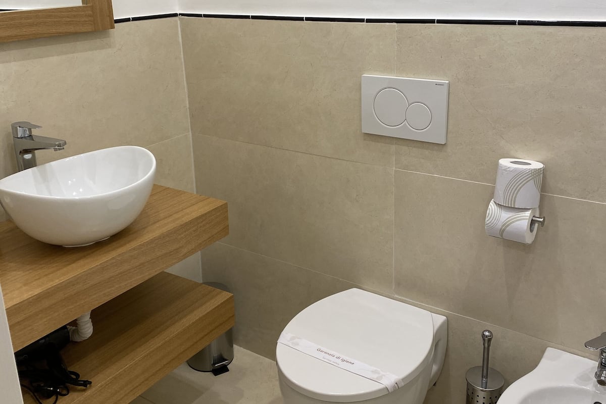 A modern bathroom with a wooden vanity, a white sink, a toilet, and a bidet.