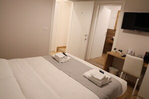 A hotel room with a bed, a desk, a TV, and a bathroom visible through an open door. - Eden Luxury Suites (Rome)