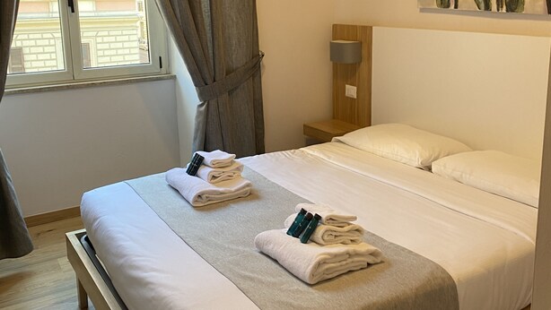 A hotel room with a bed, a painting of tulips on the wall, a window with curtains, and a nightstand with a lamp. - Eden Luxury Suites (Rome)