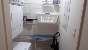 A laundry room with a washing machine, dryer, shelves with laundry baskets, and a shoe rack.