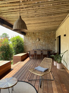 An outdoor patio with wooden flooring, a wicker chair, a round table, and a stone wall backdrop. - CASA ALTI - ARCHITECT'S HOUSE - PORTO VECCHIO (Lecci)