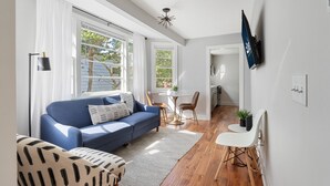 A modern living room with a blue sofa, a white armchair, and a dining area with a small table and chairs. - Casa Bella - Suite A | Downtown Beauty from 1800s (Charleston)