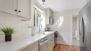 A modern kitchen with white cabinetry, a stainless steel refrigerator, and a potted plant on the counter. - Casa Bella - Suite A | Downtown Beauty from 1800s (Charleston)