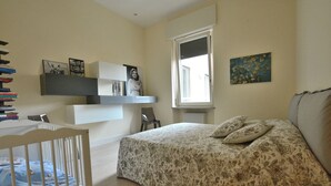 A bedroom with a bed, a crib, a window, and shelves with books and pictures. - Residenza Vecchia Veronetta (Verona)