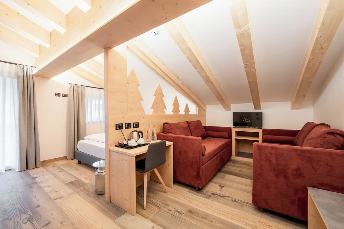 A cozy loft-style room with a bed, a desk with a chair, and a red sofa.