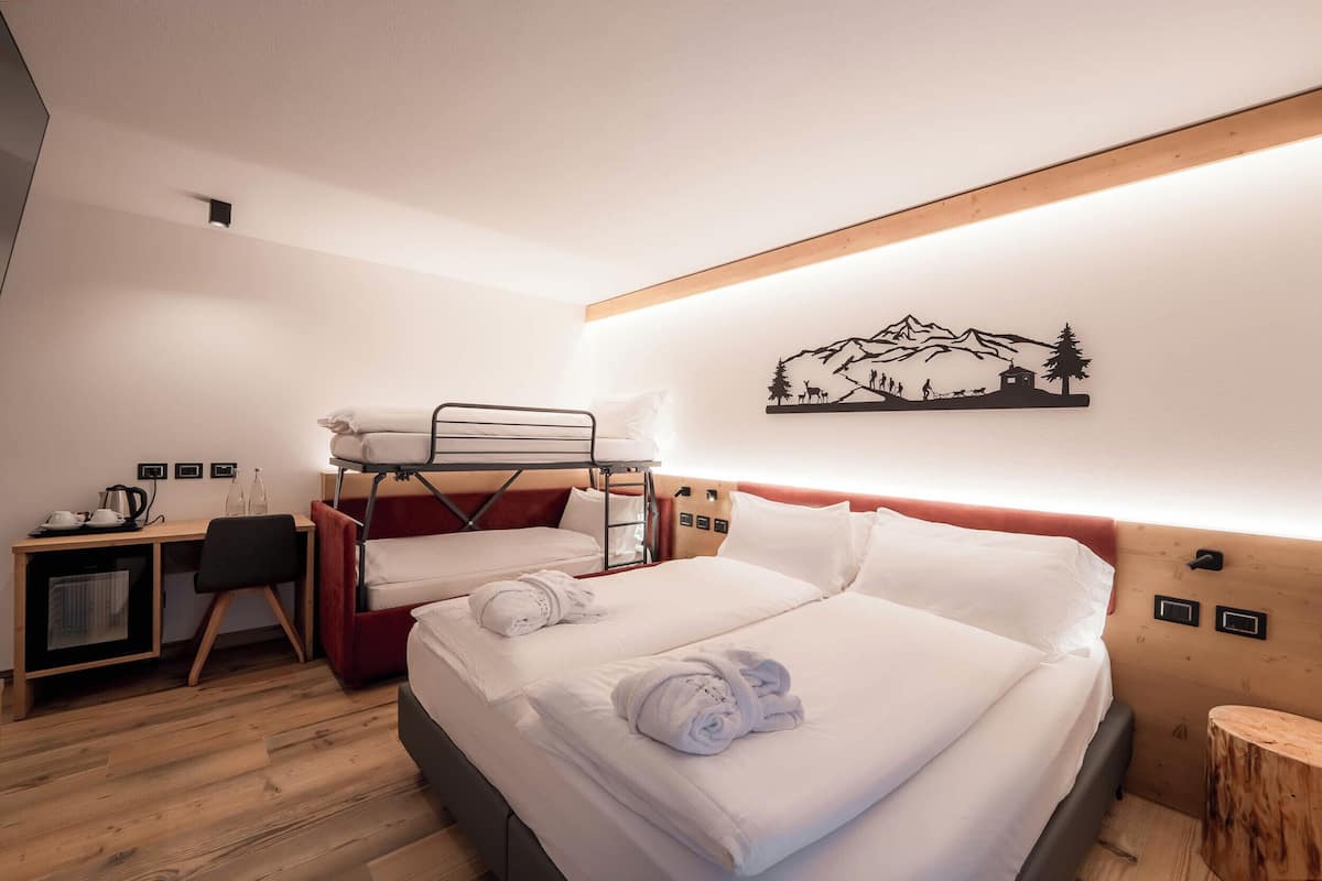 A hotel room with two beds, a desk with a chair, a small table, and a wall-mounted artwork depicting mountains.
