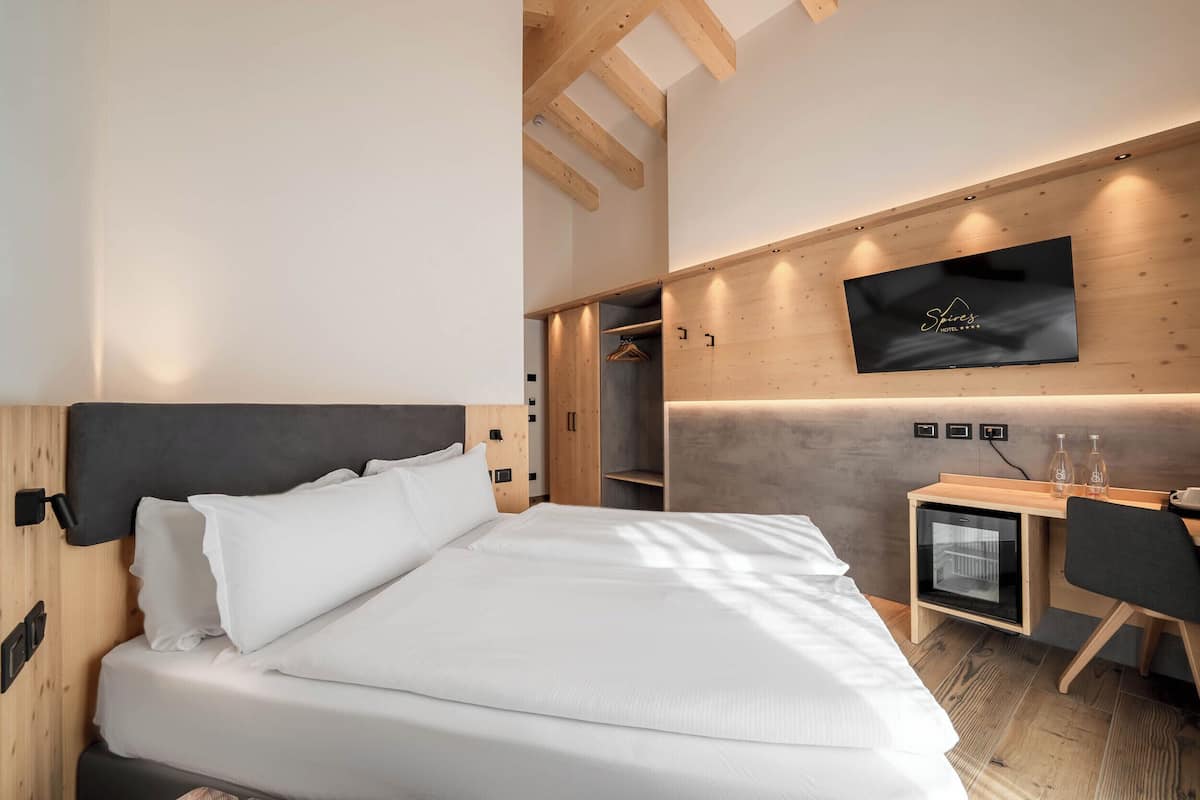 A modern hotel room with a bed, a desk, a television, and a wardrobe.