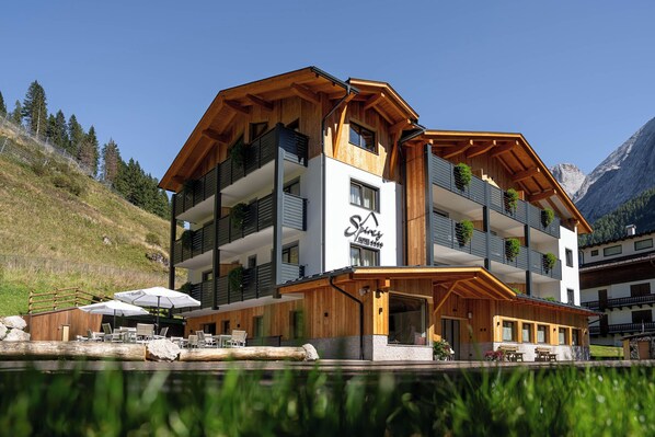 A multi-story hotel with wooden balconies, outdoor seating, and a mountain backdrop.