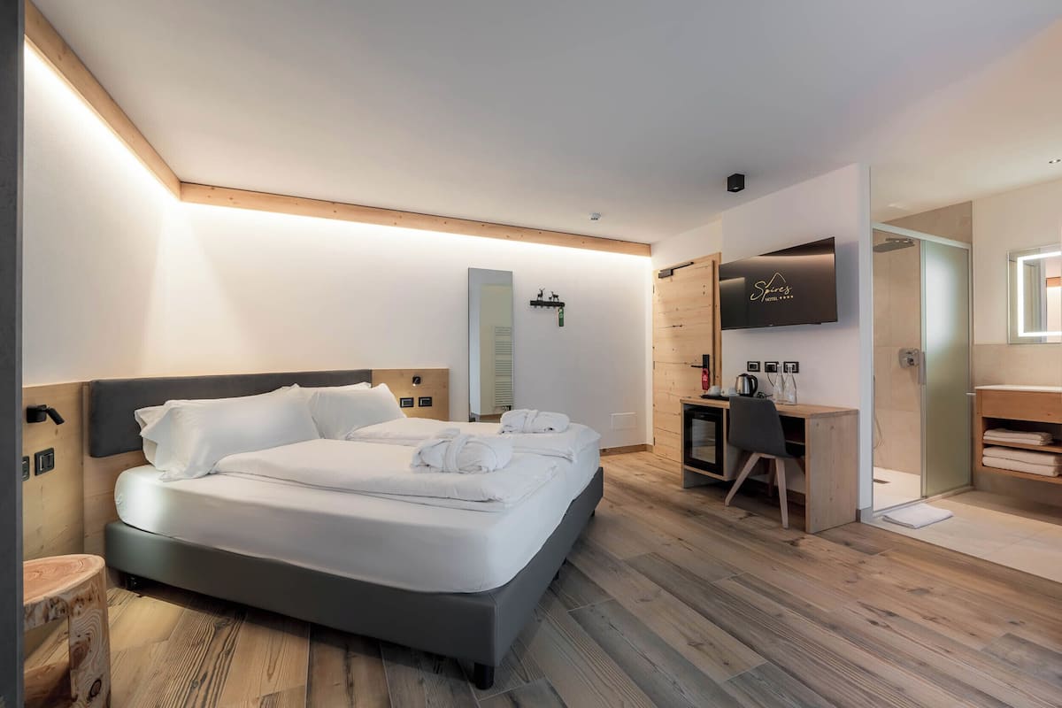 A modern hotel room with a large bed, a desk, a TV, and a shower area.