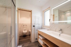 A modern bathroom with a glass shower enclosure, a wooden vanity with a mirror, and a marble-tiled wall.