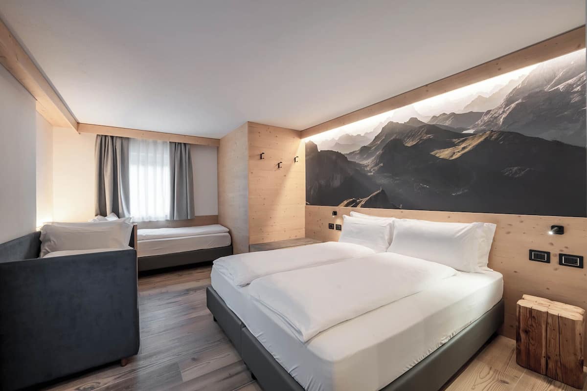 A modern hotel room with a large bed, a smaller bed, a sofa, and a wooden headboard.