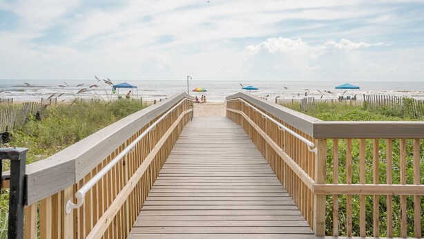 Una passerella di legno che conduce a una spiaggia con ombrelloni e una recinzione.