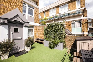 Une maison d’habitation avec un petit jardin devant, une porte grise, un banc et un mur recouvert de lierre.