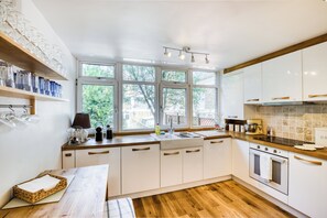 Une cuisine moderne avec des meubles blancs, un plan de travail en bois et une grande fenêtre qui laisse entrer la lumière naturelle.