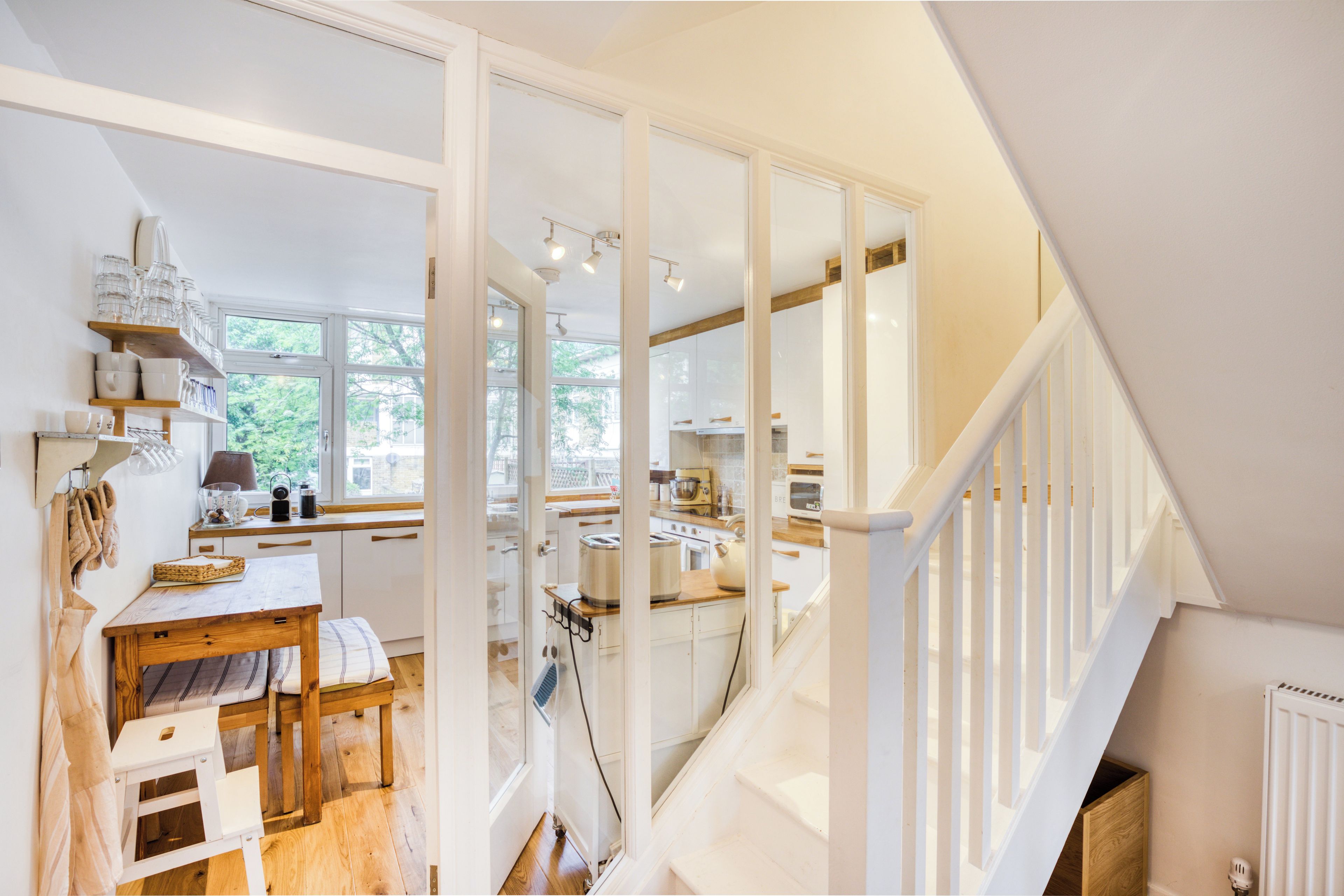 A kitchen with white cabinetry, a wooden table, and a staircase leading to another level.