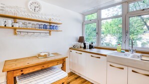 Une cuisine avec des étagères en bois, une horloge, un banc et une fenêtre donnant sur les arbres.
