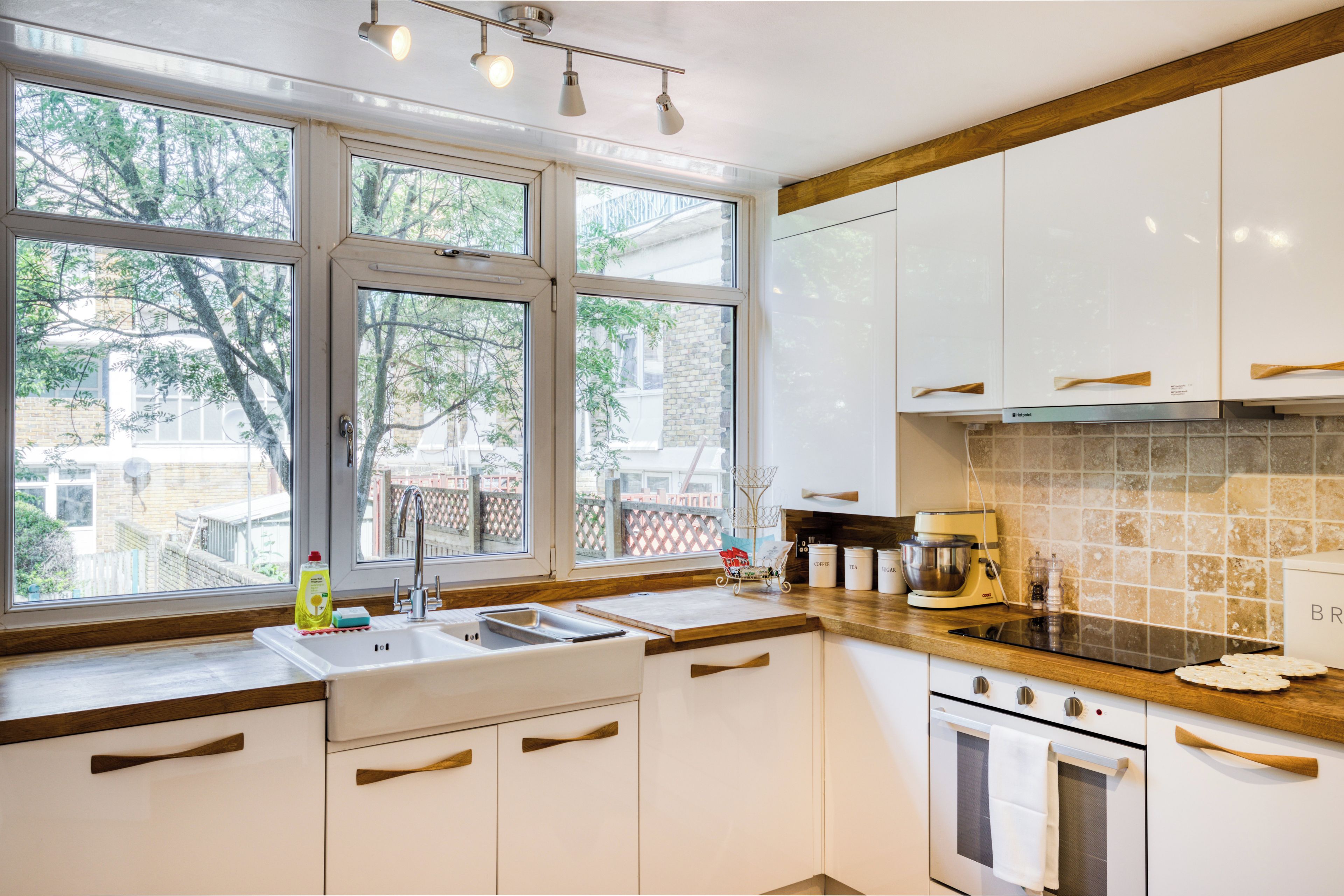 A kitchen with white cabinets, a wooden countertop, a sink, a coffee maker, and a view of the outside.