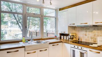 A kitchen with white cabinets, a wooden countertop, a sink, a coffee maker, and a view of the outside.