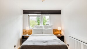 A bedroom with a bed, two bedside tables, a window, and a ceiling light fixture. - Spacious and Stylish 4BDR Home w Garden in Brixton (London)